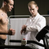 man undergoing cardiac stress test on treadmill with ECG electrodes monitored by physician