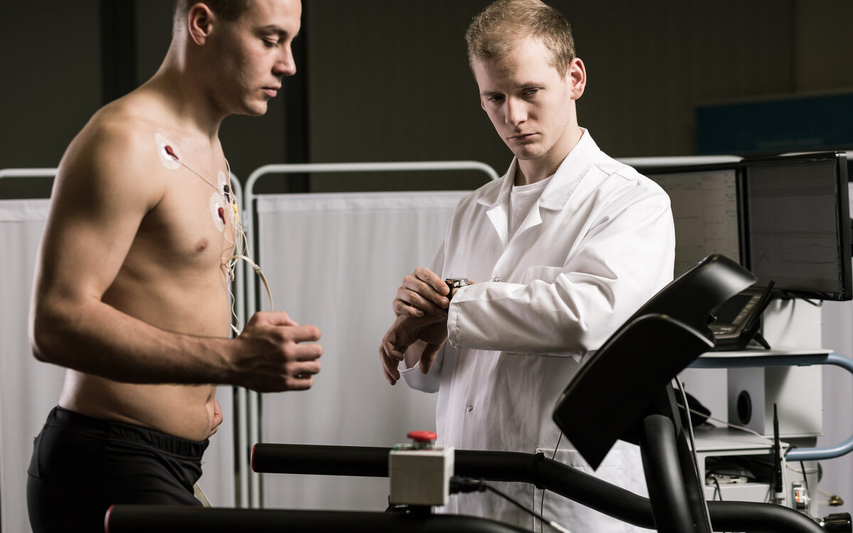 man undergoing cardiac stress test on treadmill with ECG electrodes monitored by physician
