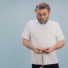 middle aged man measuring waist with tape measure concerned about low testosterone weight gain