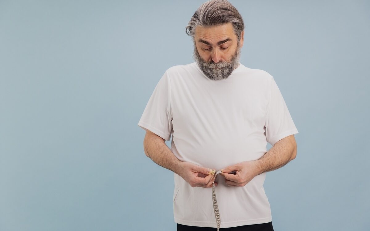 middle aged man measuring waist with tape measure concerned about low testosterone weight gain