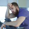 man experiencing shortness of breath during exercise leaning on gym equipment exhausted