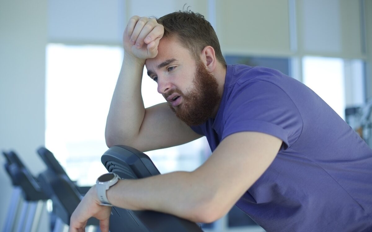 man experiencing shortness of breath during exercise leaning on gym equipment exhausted