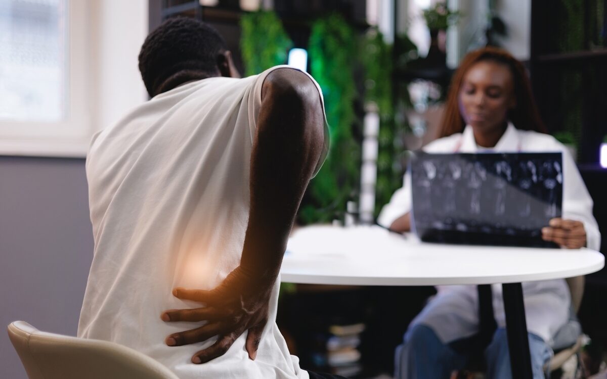 Patient holding lower back in pain during a consultation, illustrating the diagnostic step in interventional pain management