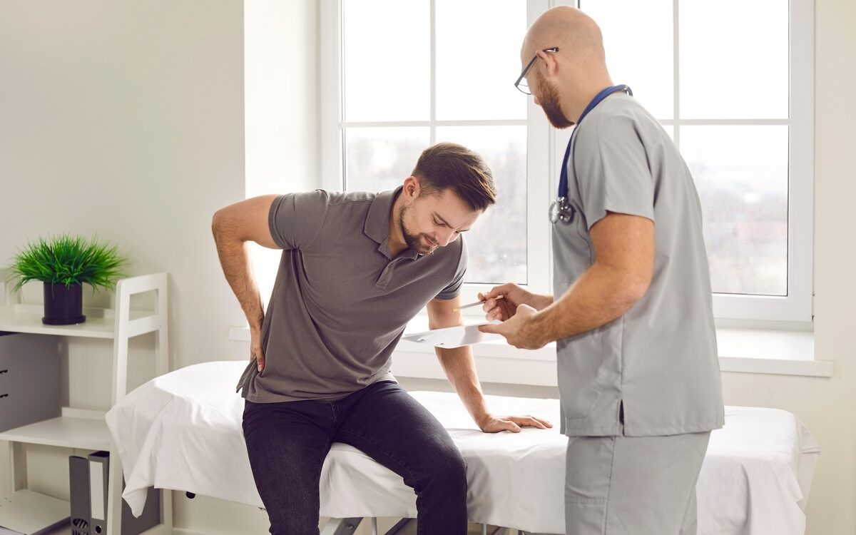 Patient holding lower back in pain during a consultation with a provider, illustrating the evaluation step for sciatica symptoms and treatment