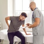 Patient holding lower back in pain during a consultation with a provider, illustrating the evaluation step for sciatica symptoms and treatment